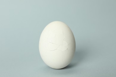 One egg with cracked shell on light grey background, closeup