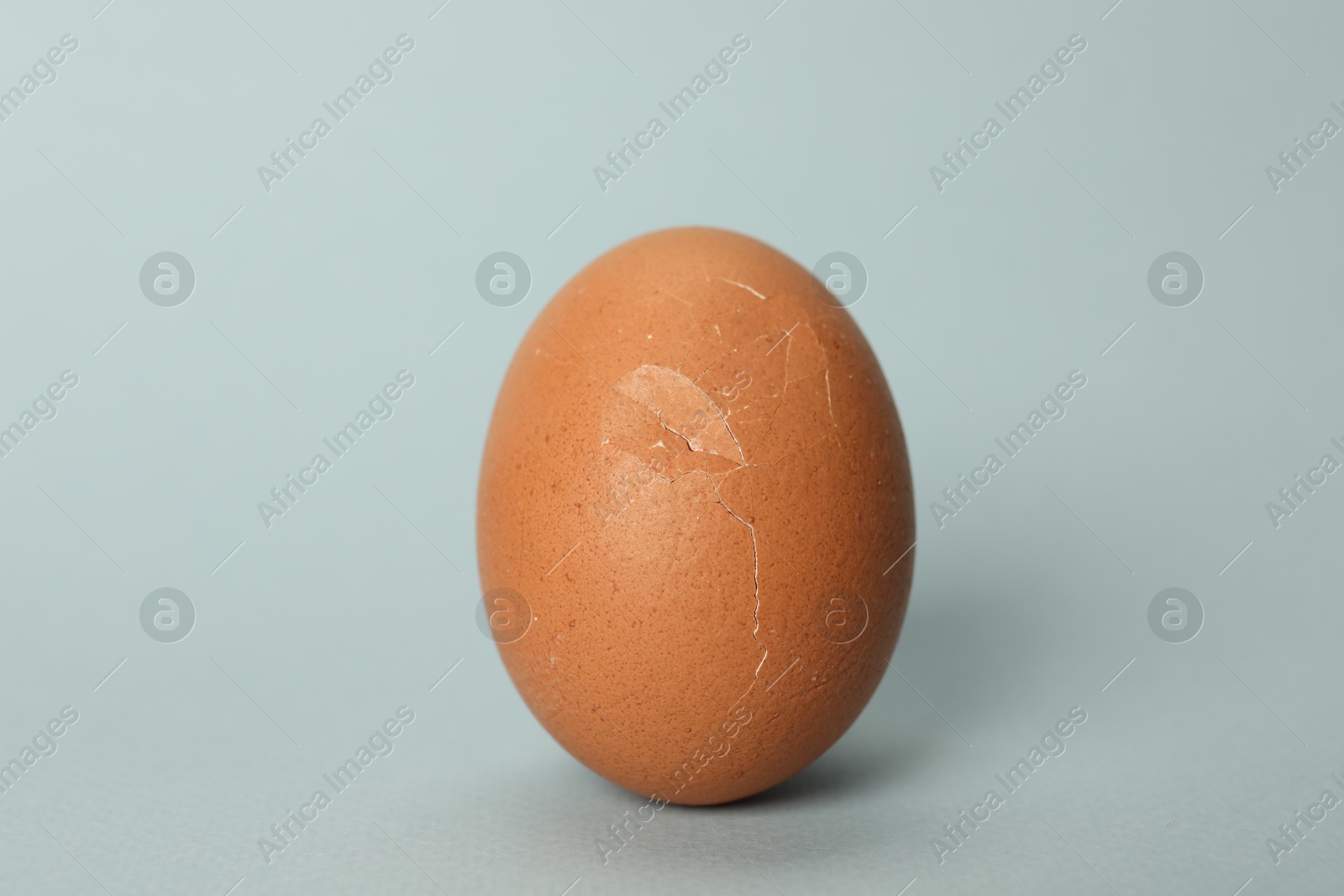 Photo of One egg with cracked shell on light grey background, closeup