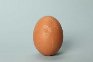 Photo of One egg with cracked shell on light grey background, closeup