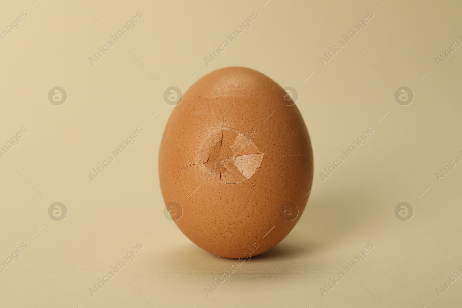 Photo of One egg with cracked shell on beige background, closeup