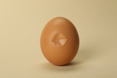 Photo of One egg with cracked shell on beige background, closeup