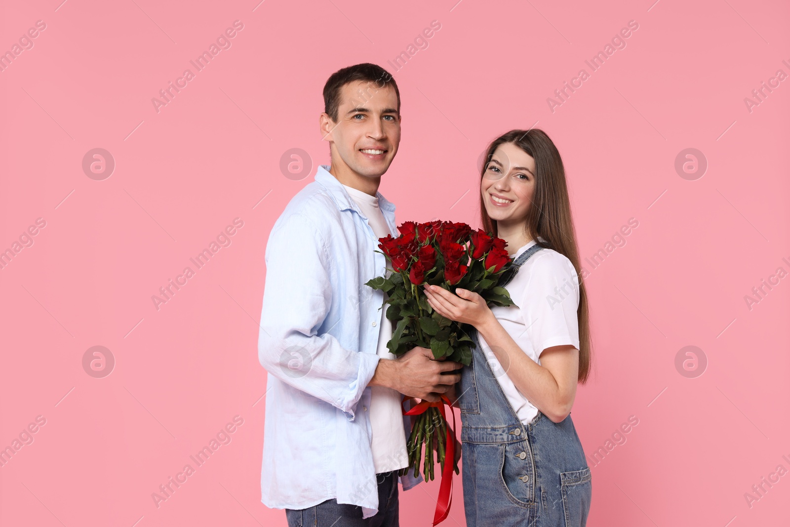 Photo of Lovely couple with bouquet of red roses on pink background. Valentine's day celebration