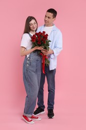 Photo of Lovely couple with bouquet of red roses on pink background. Valentine's day celebration