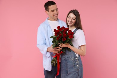 Photo of Lovely couple with bouquet of red roses on pink background. Valentine's day celebration