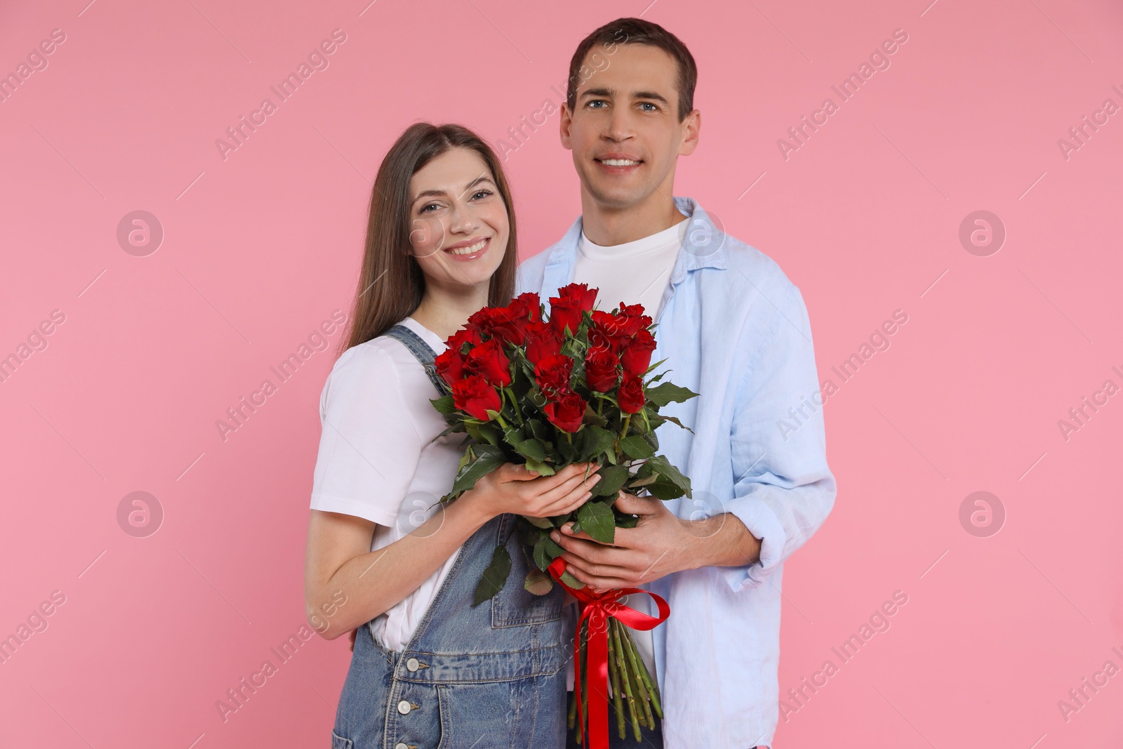 Photo of Lovely couple with bouquet of red roses on pink background. Valentine's day celebration