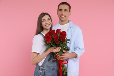 Photo of Lovely couple with bouquet of red roses on pink background. Valentine's day celebration