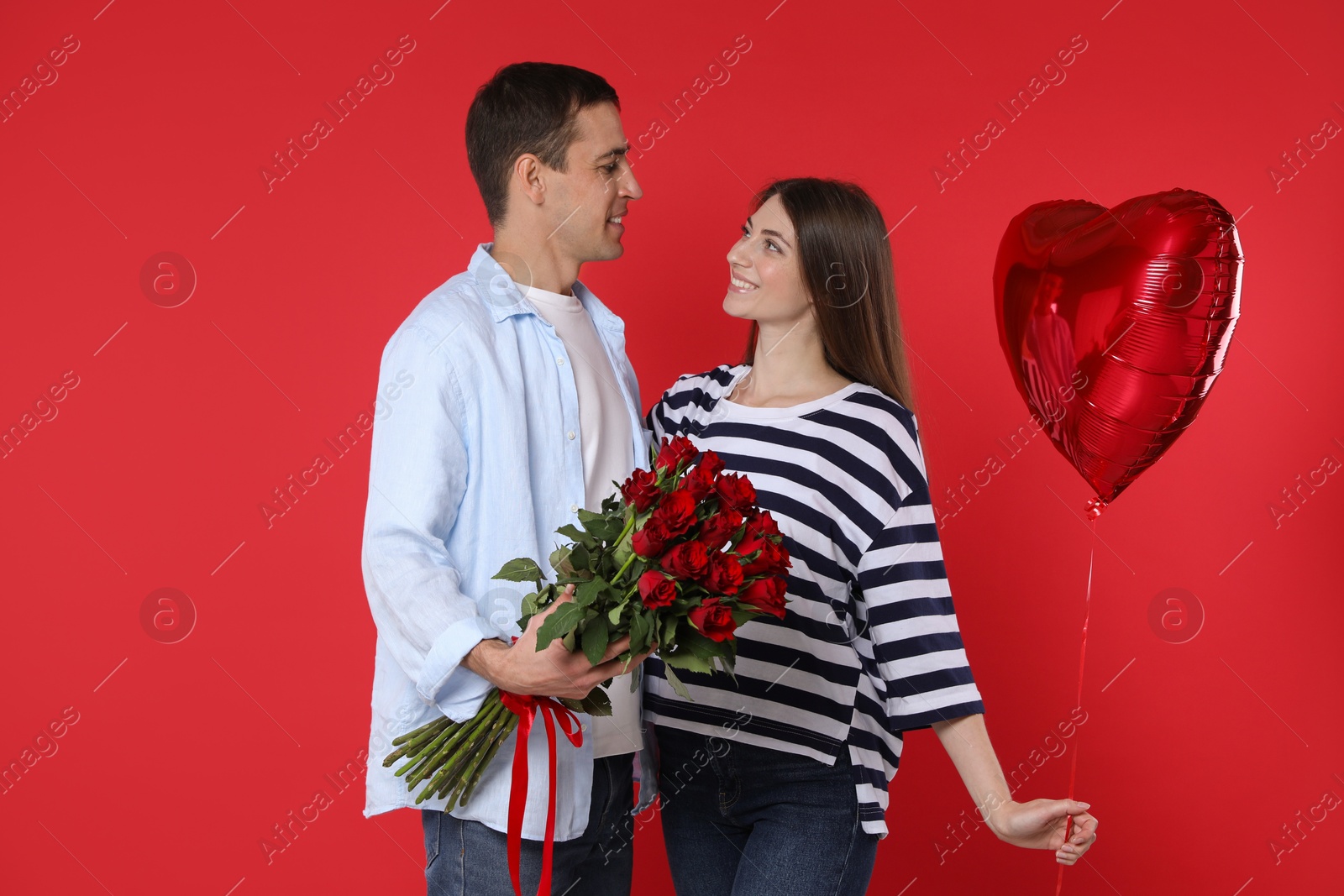 Photo of Lovely couple with bouquet of roses and heart shaped balloon on red background. Valentine's day celebration