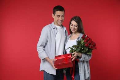 Photo of Lovely couple with bouquet of roses and gift box on red background. Valentine's day celebration