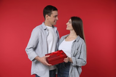 Photo of Lovely couple with gift box on red background. Valentine's day celebration