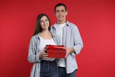 Photo of Lovely couple with gift box on red background. Valentine's day celebration