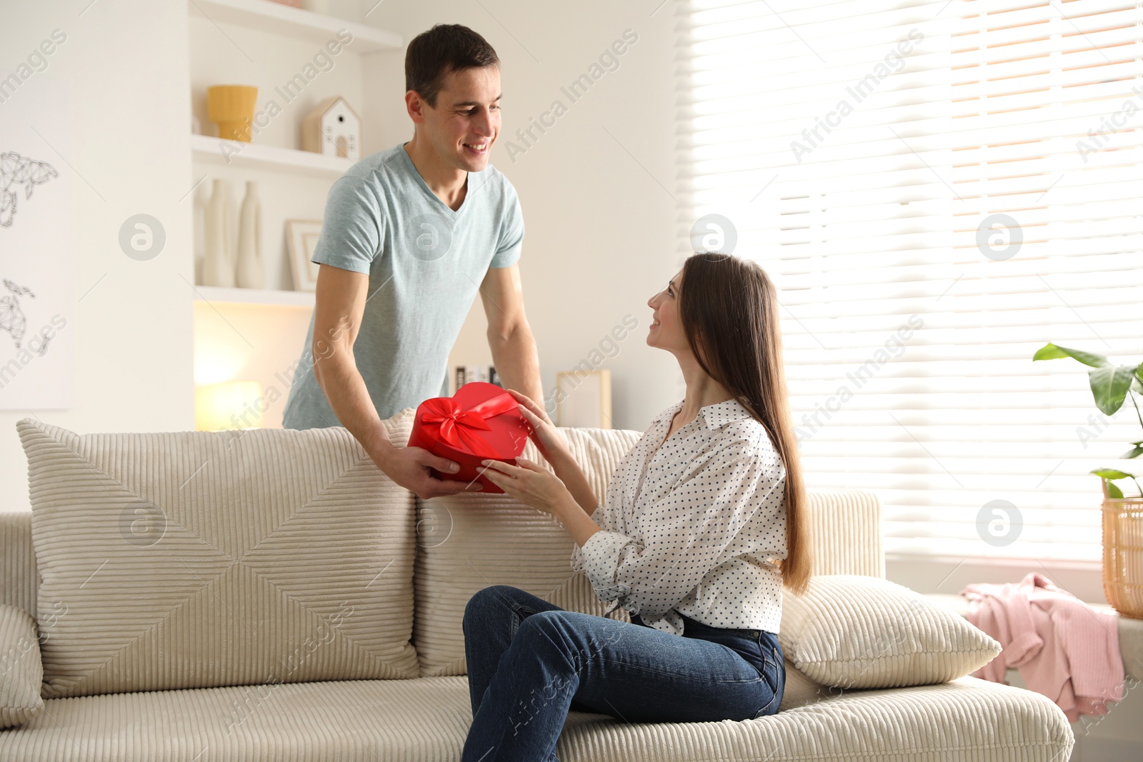 Photo of Lovely man surprising his girlfriend with Valentine's day gift indoors