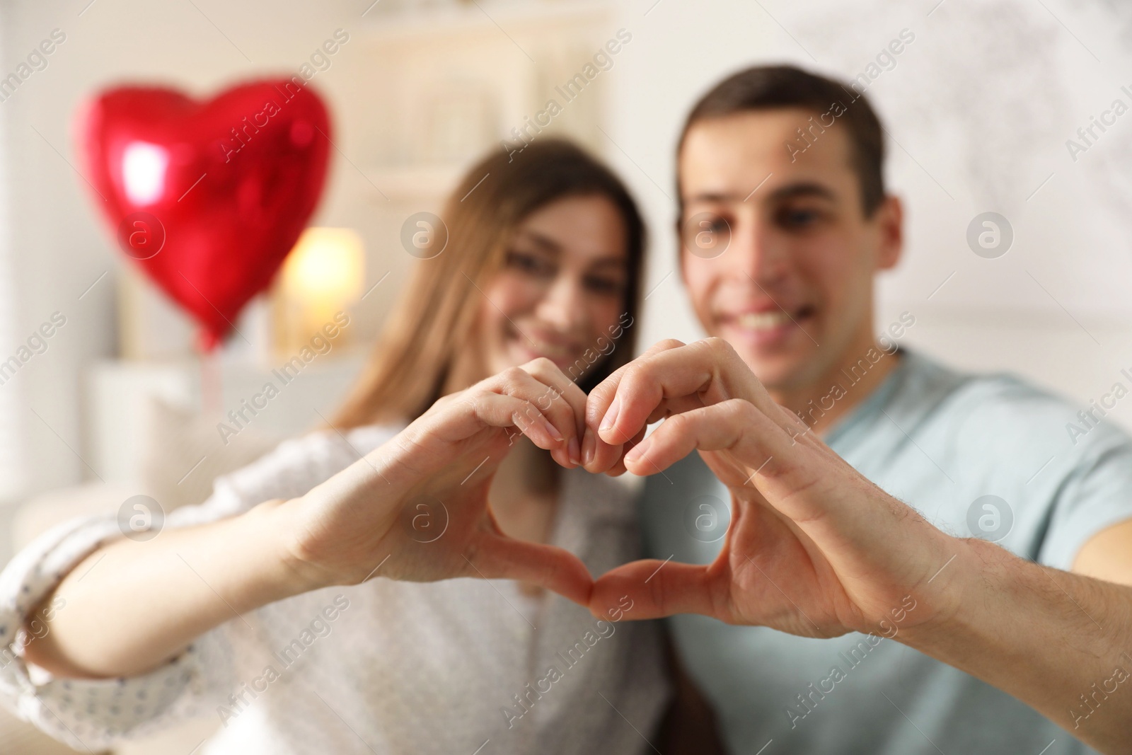 Photo of Lovely couple making heart with hands indoors, selective focus. Valentine's day celebration