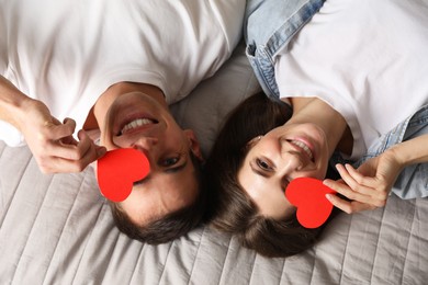 Photo of Lovely couple with paper hearts on bed, top view. Valentine's day celebration