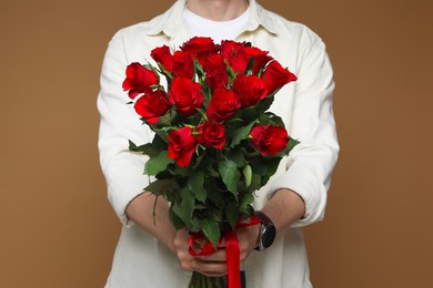 Photo of Happy Valentine's Day. Man with bouquet of roses on brown background, closeup