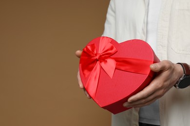 Photo of Happy Valentine's Day. Man with heart shaped gift box on brown background, closeup. Space for text