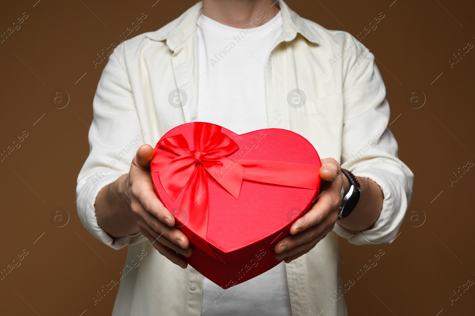 Photo of Happy Valentine's Day. Man with heart shaped gift box on brown background, closeup