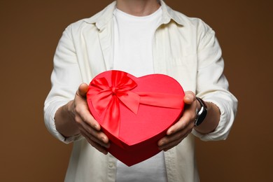 Photo of Happy Valentine's Day. Man with heart shaped gift box on brown background, closeup