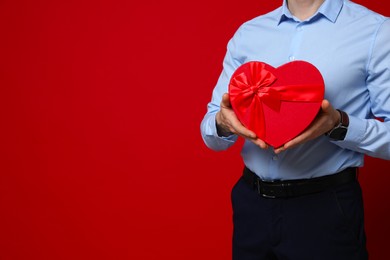 Photo of Happy Valentine's Day. Man with heart shaped gift box on red background, closeup. Space for text