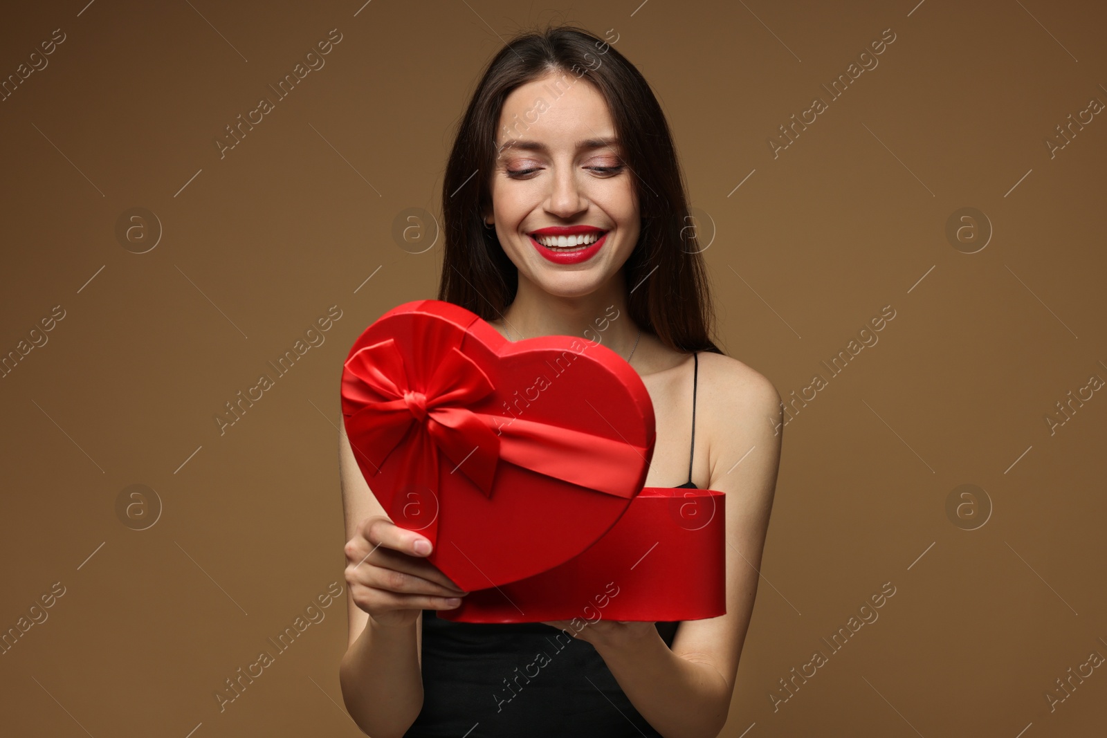 Photo of Happy Valentine's Day. Beautiful woman opening gift on brown background