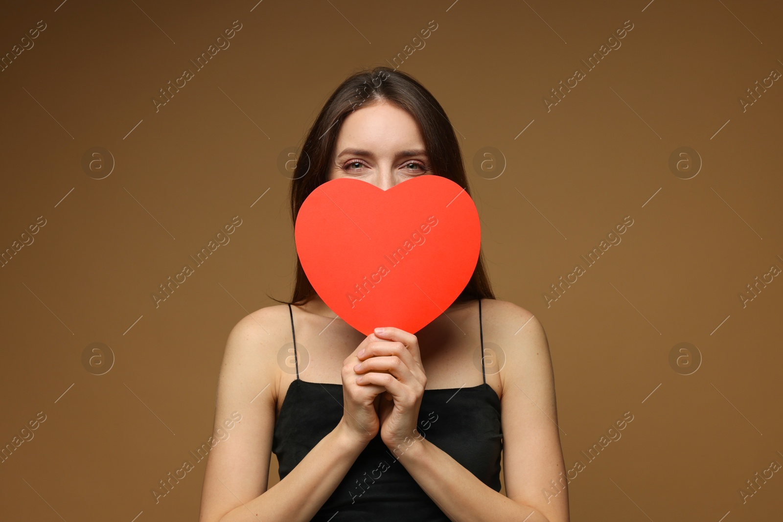 Photo of Happy Valentine's Day. Woman hiding behind paper heart on brown background