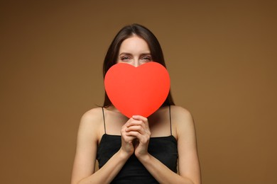 Photo of Happy Valentine's Day. Woman hiding behind paper heart on brown background