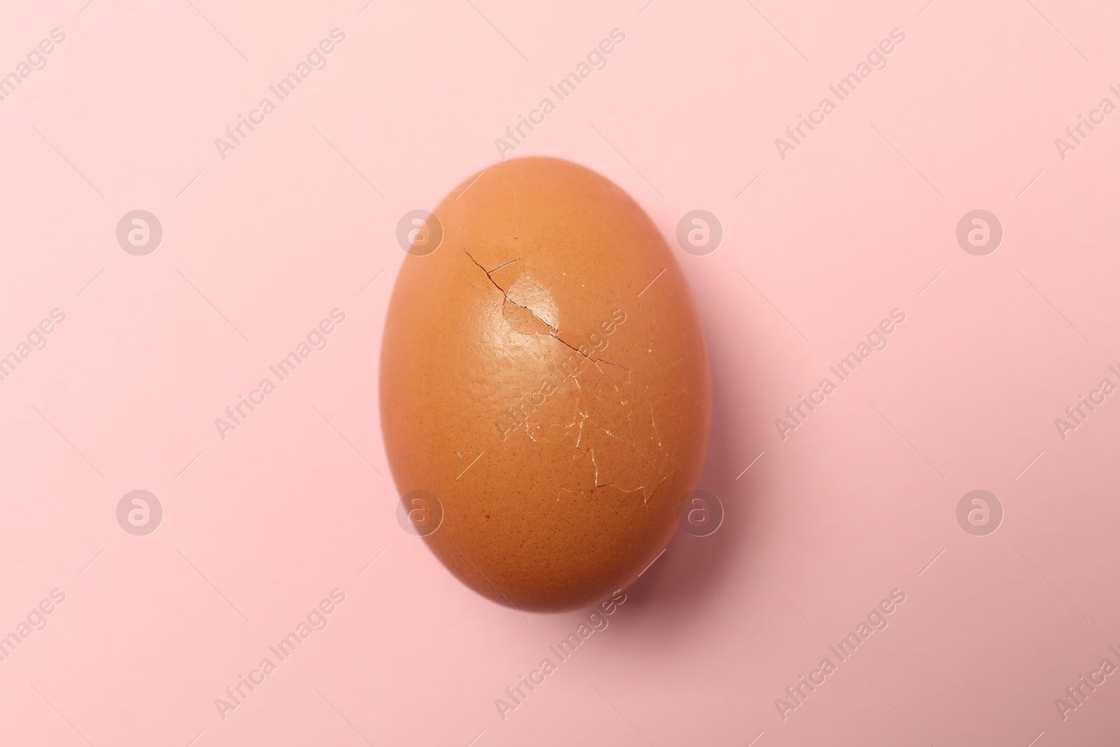 Photo of One egg with cracked shell on pink background, top view