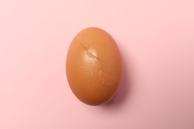 One egg with cracked shell on pink background, top view