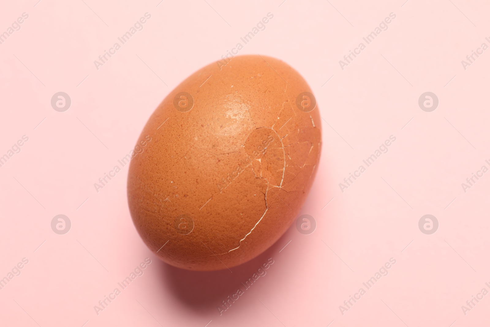 Photo of One egg with cracked shell on pink background, closeup