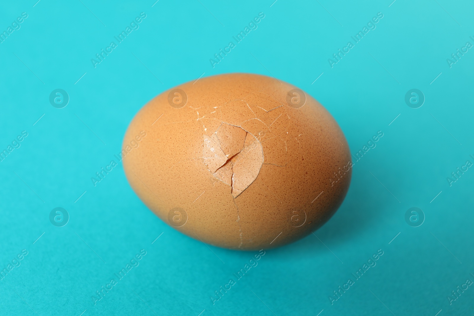 Photo of One egg with cracked shell on light blue background, closeup