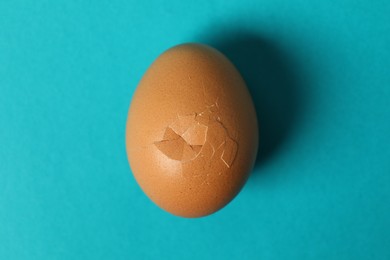 Photo of One egg with cracked shell on light blue background, top view