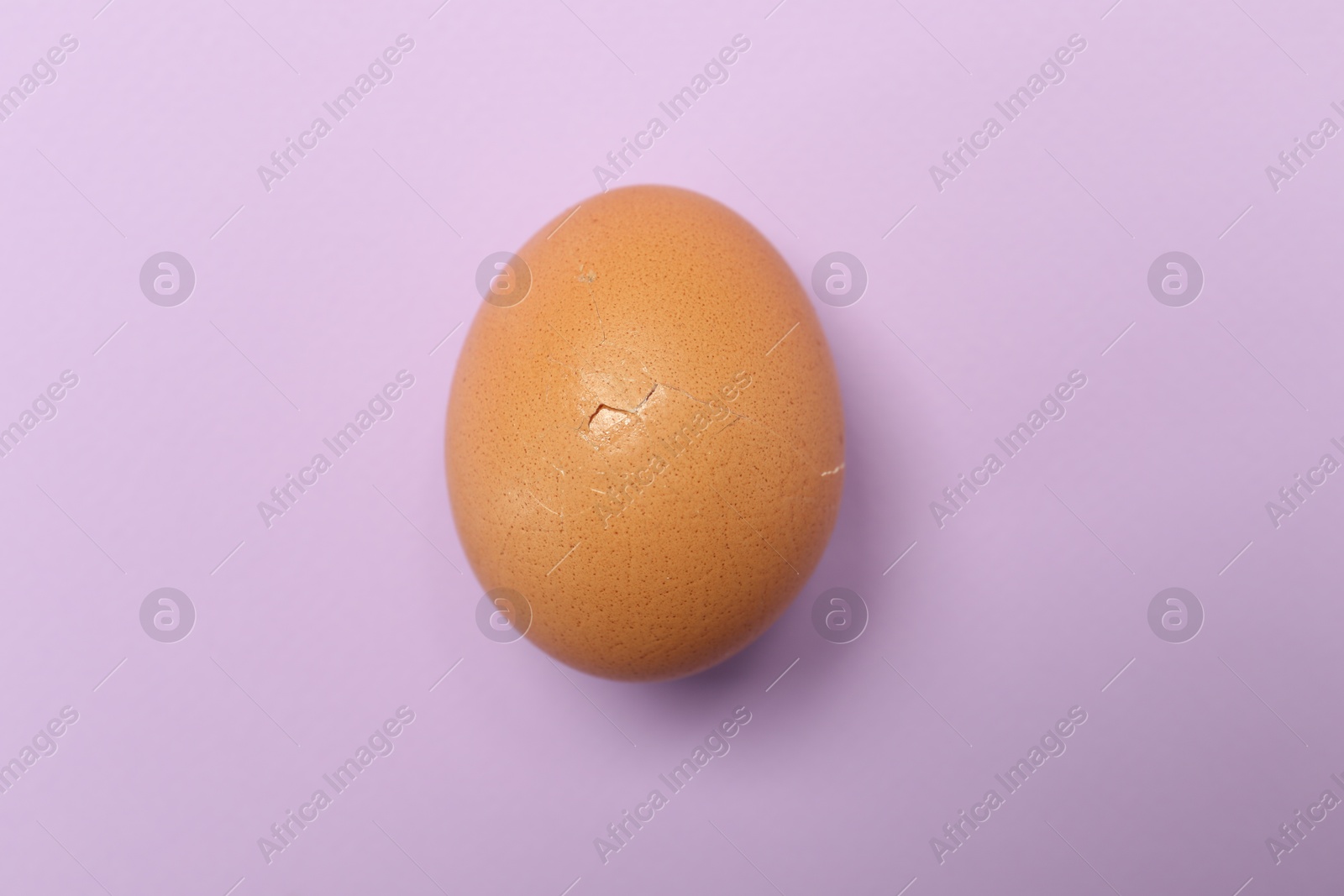 Photo of One egg with cracked shell on violet background, top view