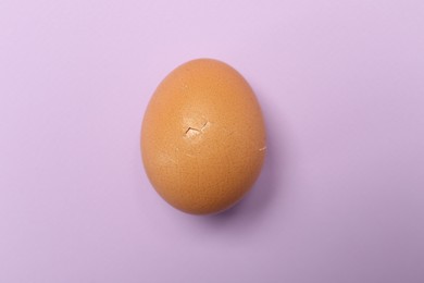 One egg with cracked shell on violet background, top view