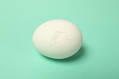 Photo of One egg with cracked shell on turquoise background, closeup