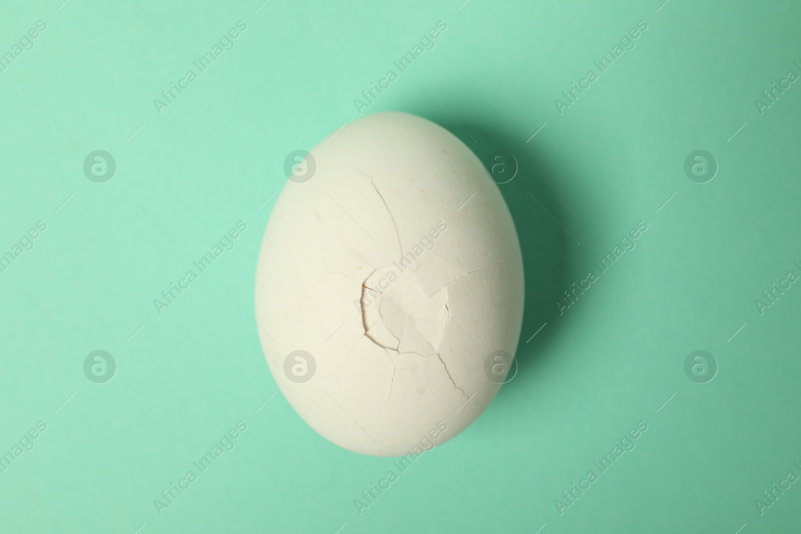 Photo of One egg with cracked shell on turquoise background, top view