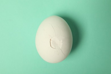 Photo of One egg with cracked shell on turquoise background, top view