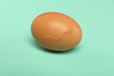 Photo of One egg with cracked shell on turquoise background, closeup