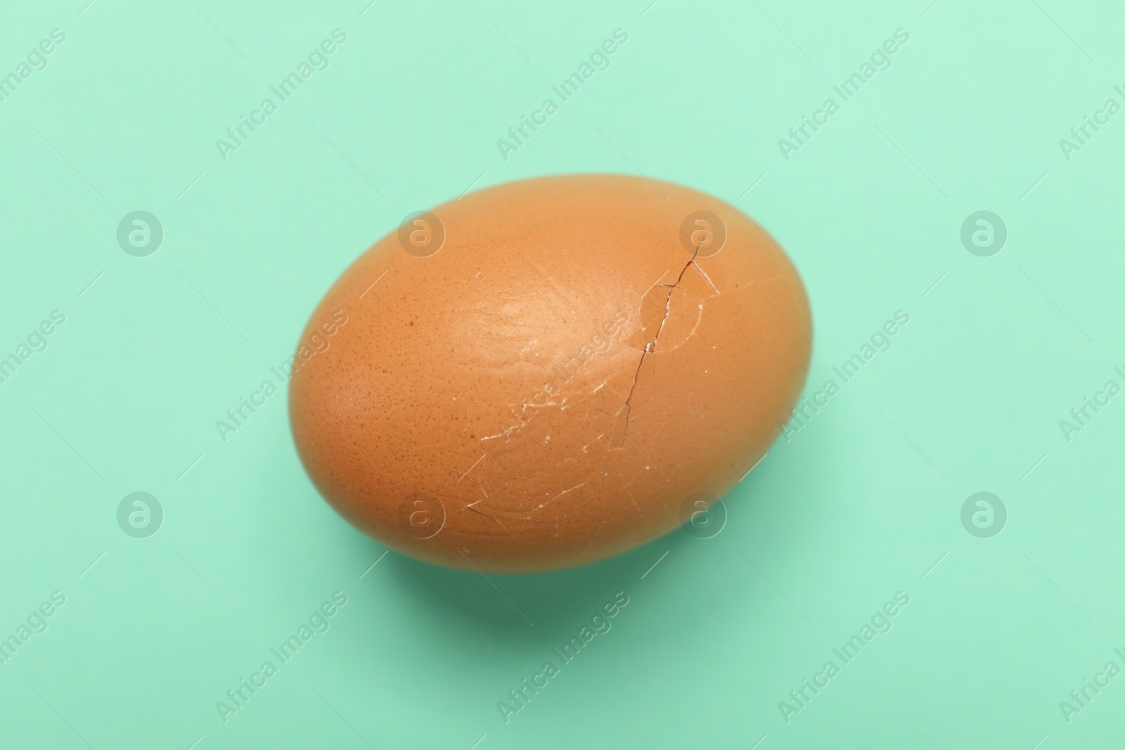 Photo of One egg with cracked shell on turquoise background, top view