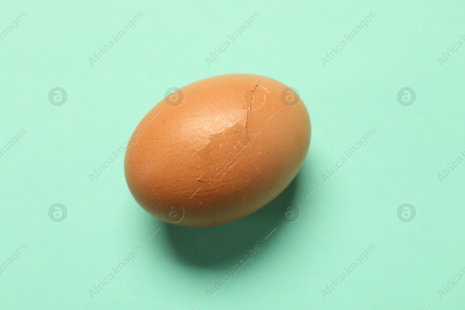 Photo of One egg with cracked shell on turquoise background, top view