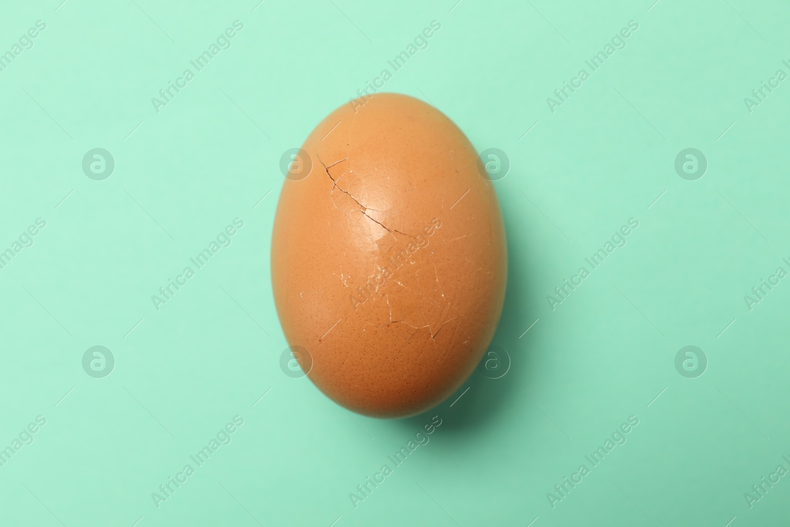 Photo of One egg with cracked shell on turquoise background, top view