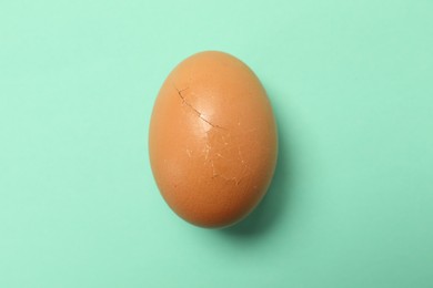 One egg with cracked shell on turquoise background, top view