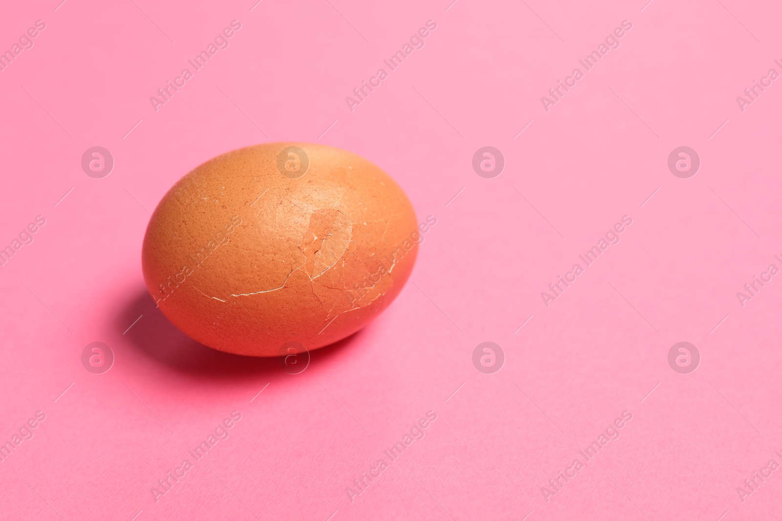 Photo of One egg with cracked shell on pink background, space for text