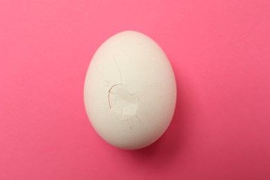 Photo of One egg with cracked shell on pink background, top view