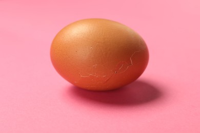 Photo of One egg with cracked shell on pink background, closeup