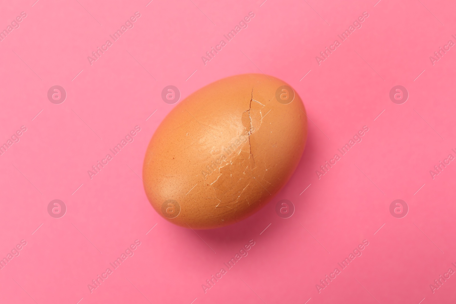 Photo of One egg with cracked shell on pink background, top view