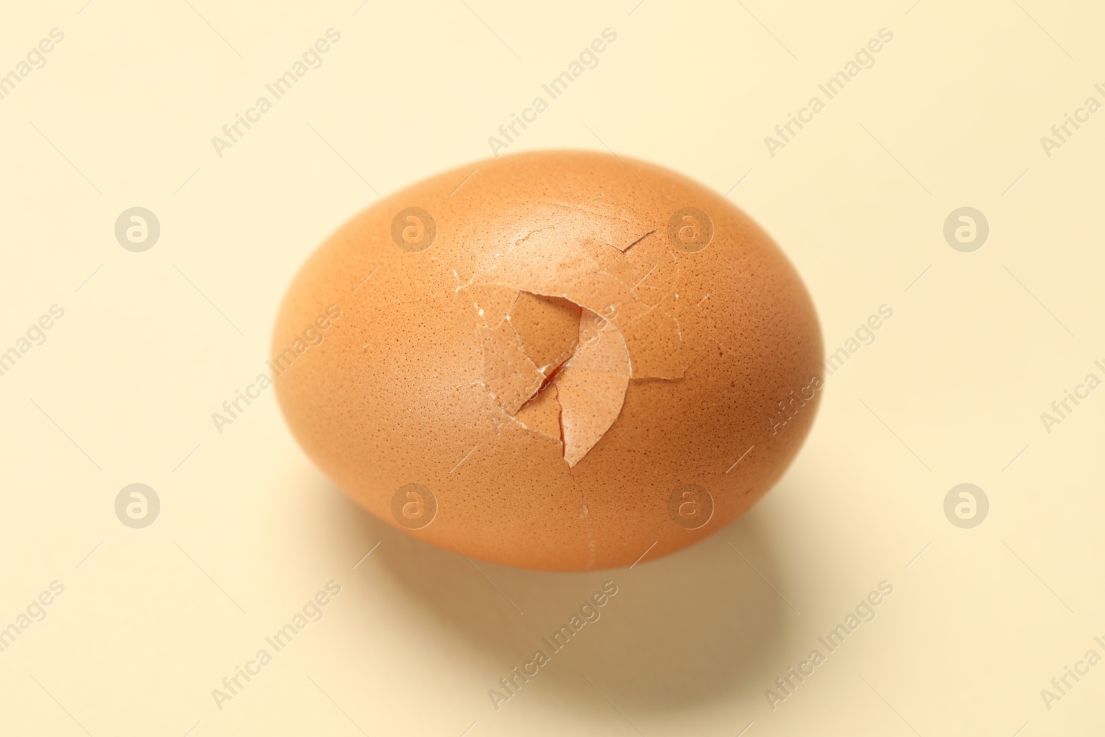 Photo of One egg with cracked shell on beige background, closeup