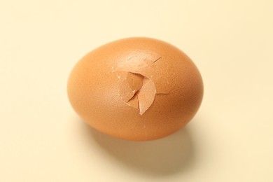 One egg with cracked shell on beige background, closeup