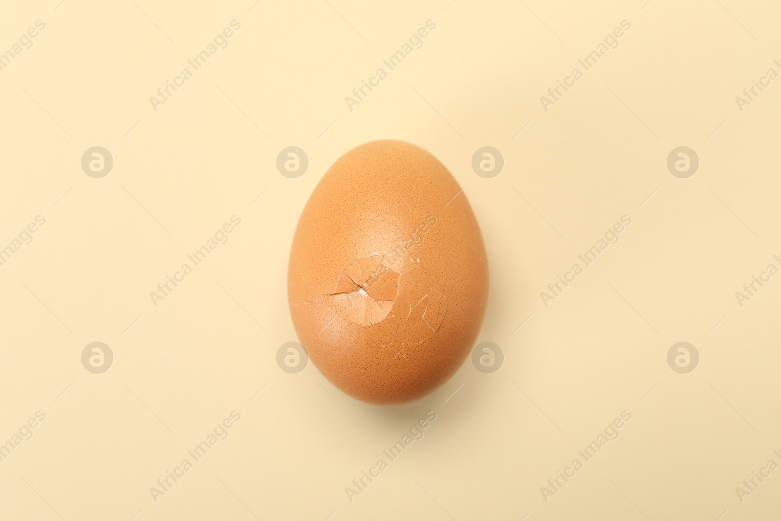 Photo of One egg with cracked shell on beige background, top view