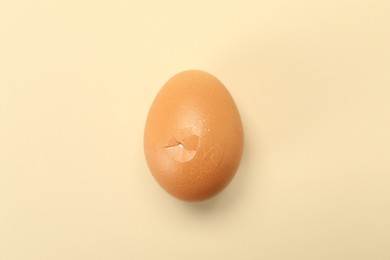 Photo of One egg with cracked shell on beige background, top view