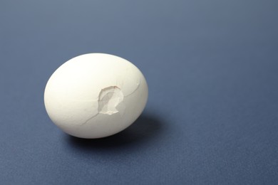 Photo of One egg with cracked shell on blue background, space for text