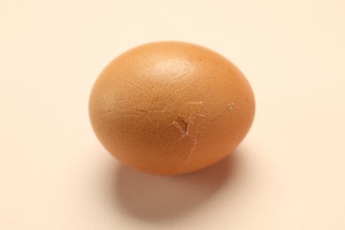 One egg with cracked shell on beige background, closeup